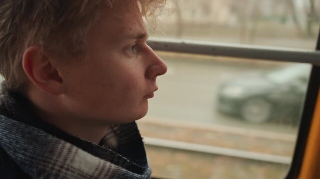 Introspective white male creator looking outside holding hat in lap, eyes tracking traffic and storefronts through rainstreaked glass, overcast light and shallow depth, contemplative filmmaker mood,