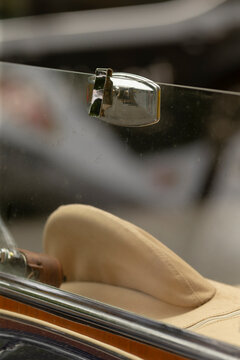 Close-up view of a vintage car interior showing a beige leather seat cushion, a polished chrome window latch attached to a frameless glass window, and part