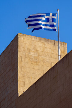 Greek flag flies over a stone building under a clear blue sky during the day