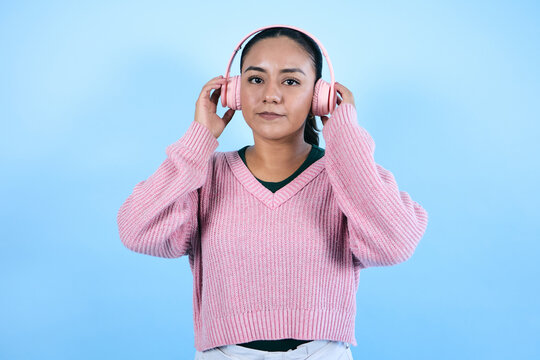 young mexican woman listening to music and using headphones on blue background in Mexico Latin America, Latina young brunette girl portrait