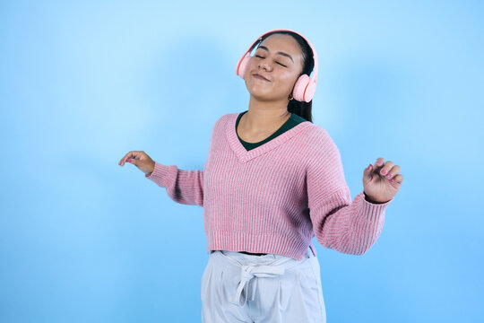 young mexican woman listening to music and using headphones on blue background in Mexico Latin America, Latina young brunette girl portrait