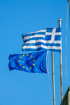 Two flags flying together representing Greece and the European Union against a clear blue sky