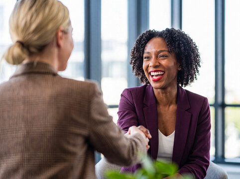 Happy young African American businesswoman laughing and shaking hands with a colleague in a bright modern office.
