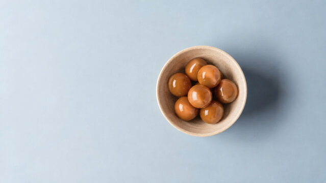 Caramel Candies in Bowl: A small wooden bowl filled with glistening caramel candies sits on a cool, pale blue surface, inviting a sweet indulgence.