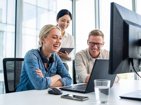 Cheerful diverse business team collaborating and sharing laughter while working on computers in a modern office.
