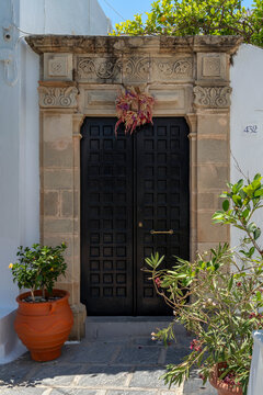 Black door with decorative stone frame and plants in pots in Lindos
