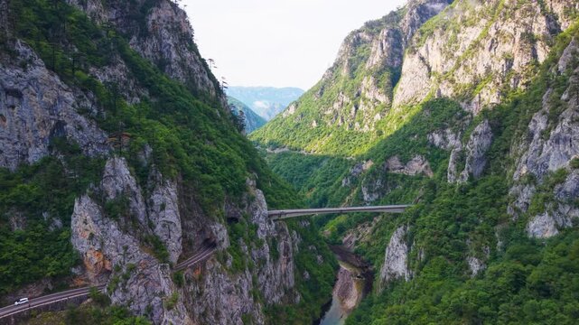 Aerial view of cars driving across a bridge into a rock tunnel in Piva River canyon near Montenegro border