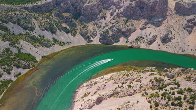 Breathtaking aerial view of Zrmanja River canyon meander with a speedboat navigating emerald waters in Croatia