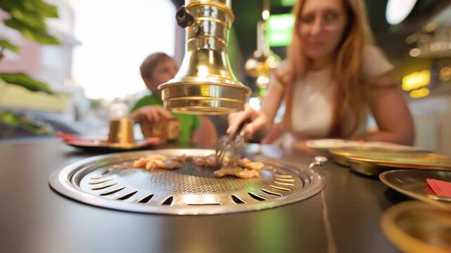 Family cooking meat at korean barbecue restaurant table