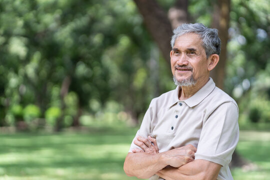 elderly pensioner man spend leisure time relaxing in green park,standing crossed arms in the nature atmosphere