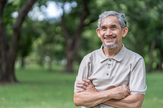 elderly pensioner man spend leisure time relaxing in green park,standing crossed arms in the nature atmosphere