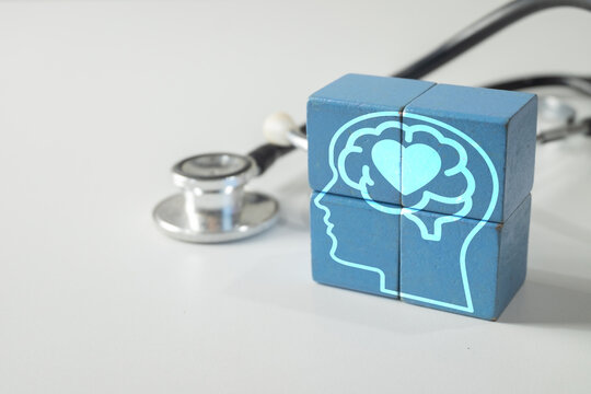 Mental health diagnosis and psychological care concept. Blue wooden blocks with a digital human head, brain, and heart graphic next to a stethoscope on a white background.