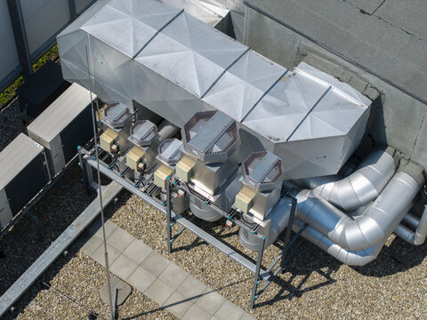 Aerial view of a mechanical ventilation system with metal ducts and fans installed on a gravel rooftop in Krakow, Poland.