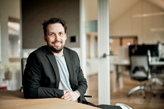 A smiling businessman sits at a desk in a modern office