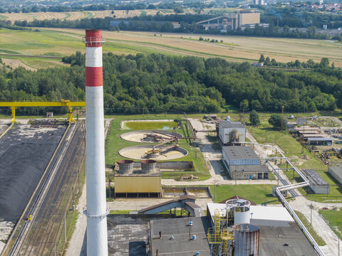 Aerial view of sugar refinery technical installations featuring a tall chimney, circular water treatment tanks, and industrial buildings surrounded by green fields in Poland.