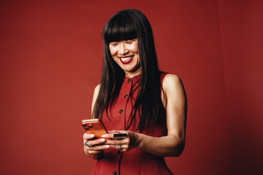 Mature woman texting on smartphone in studio against a red background