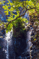 A shimmering waterfall cascades over dark, wet rocks © wundermann