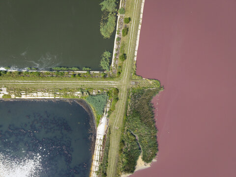 Aerial view of sugar refinery sedimentation ponds with contrasting dark green and reddish water separated by a dirt embankment in Poland.