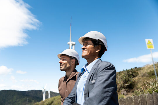Male engineers wear helmets near a wind turbine outdoors in Ecuador
