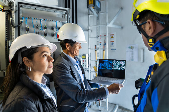 An engineer and a technician watch a laptop inside a wind turbine