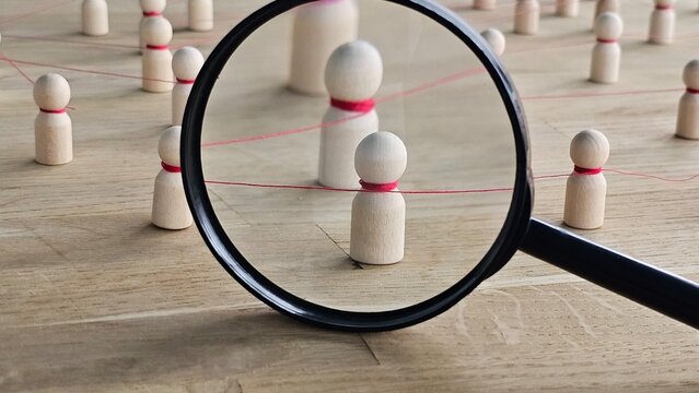 Looking through a magnifying glass at wooden figures connected by red string