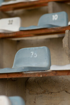 Close-up view of aged gray plastic spectator seats with faded white numbers mounted on rusty metal frames and weathered concrete steps, shallow depth of field