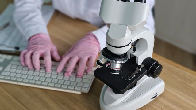 Scientist uses microscope while typing on keyboard in laboratory