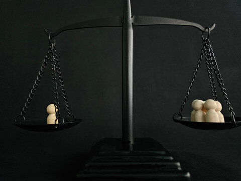 Two groups of figures on balance scales represent different sides of an issue in a dark