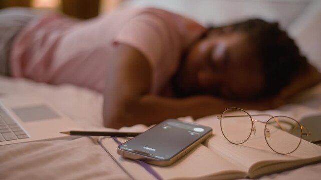 Tired African American woman sleeping missing mobile phone call receiving missed notification beside book and glasses at home bedroom exhausted female student girl napping late night studying rest