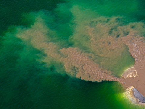 Aerial view of a post-industrial lake in Poland, showing a plume of sediment-rich water mixing with the clear green lake water.