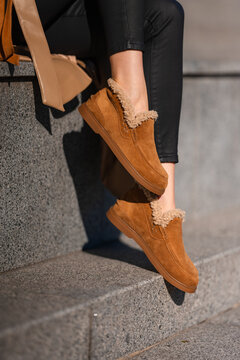 Tan suede ankle boots with shearling trim resting on sunlit stone steps beside black leggings, showing cozy urban style, textured surfaces, relaxed cold-weather fashion