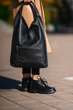 person holding black leather bag in casual outdoor setting with tan coat and black pants close-up view on paved surface period period period period period period period period period period.
