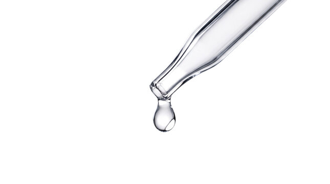 A clear liquid drop falling from a glass pipette on transparent background