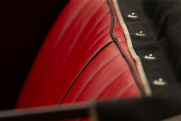 Obraz premium Tight view of a red leather automobile seat featuring vertical quilting, black piping trim, and adjacent black fabric with chrome snap fasteners. Warm