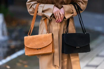 Beige trench coat styled on woman holding orange and black handbags with urban fashion pose and visible accessory details for street style concept, with handbag, fashion, woman, coat detail © flywish