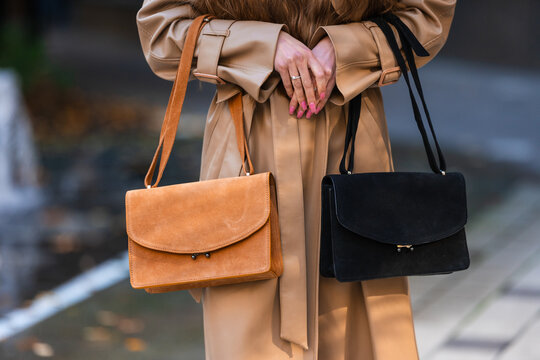 Beige trench coat styled on woman holding orange and black handbags with urban fashion pose and visible accessory details for street style concept, with handbag, fashion, woman, coat detail