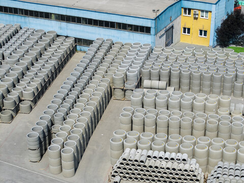Aerial view of Bruk-Bet concrete pipe stacks arranged in rows at an industrial facility with a blue and yellow building in the background in Poland.