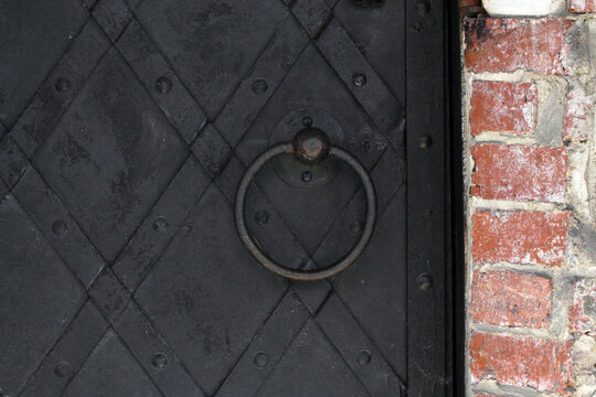 Close-up of historic building fragment with massive wrought iron door and round cast iron handle, old architectural detail