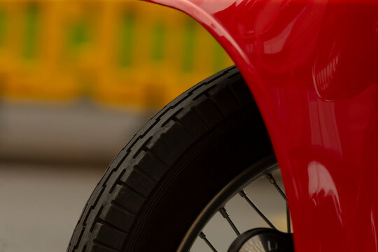 Tight crop showing a black motorcycle tire and spoke wheel partially covered by a glossy red fender. The scene features shallow depth of field with a blurred