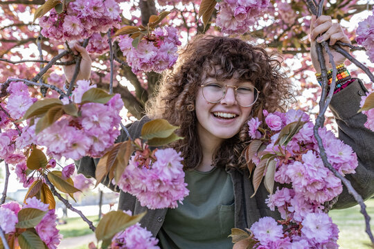 A happy teenager holds a cherry blossom branch outdoors in spring