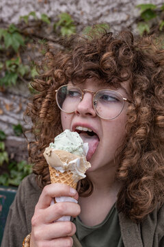Teenage girl with glasses licks an ice cream cone outdoors