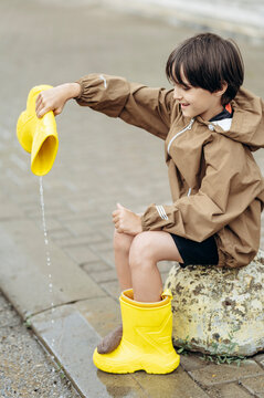 Smiling boy pours water from his yellow rain boot