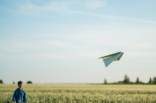 Boy throws a paper airplane in a summer field