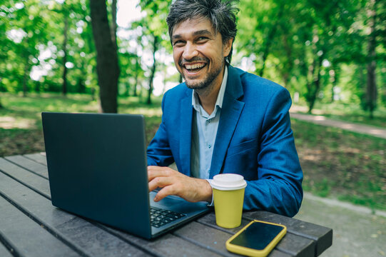 Smiling businessman works on a laptop at an outdoor park table