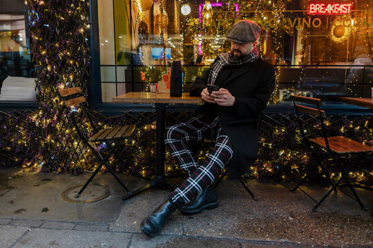 Stylish man uses smartphone at an outdoor cafe in winter