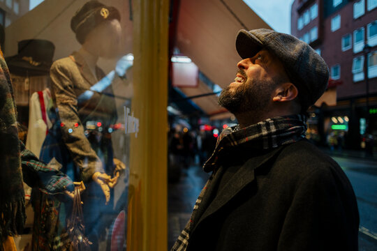 A smiling man in a flat cap looks at a vintage shop window display