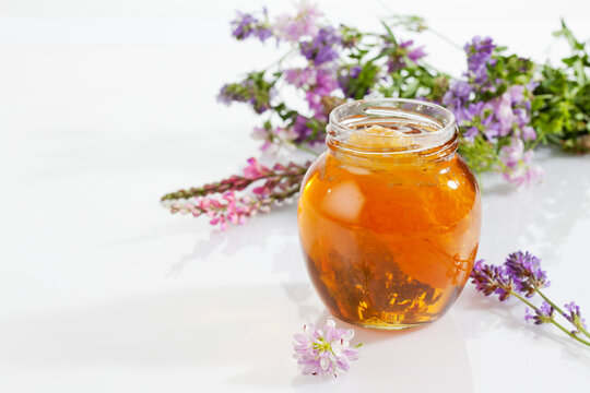 Glass of blossom honey with honeycomb and blossoms on white ground