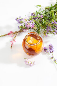Glass of blossom honey with honeycomb and blossoms on white ground