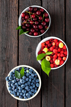 Three bowls of sour cherries, raspberries and blueberries on dark wood