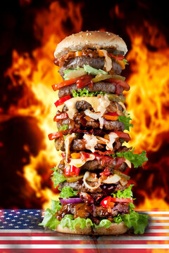 Extra large hamburger on US flag against burning flalmes